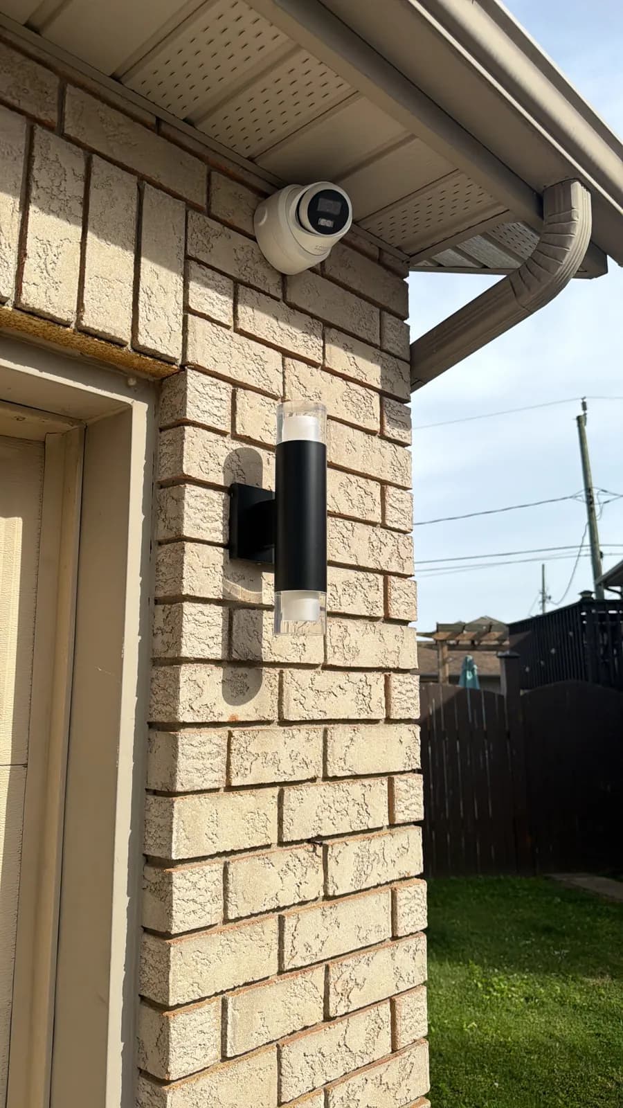 Turret camera mounted under the eave above a side door of a brick home